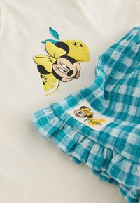 Minnie Mouse se žlutou mašlí a potiskem citronů na bílé tkanině vedle modré kostkované látky s volánky a nášivkou Minnie.