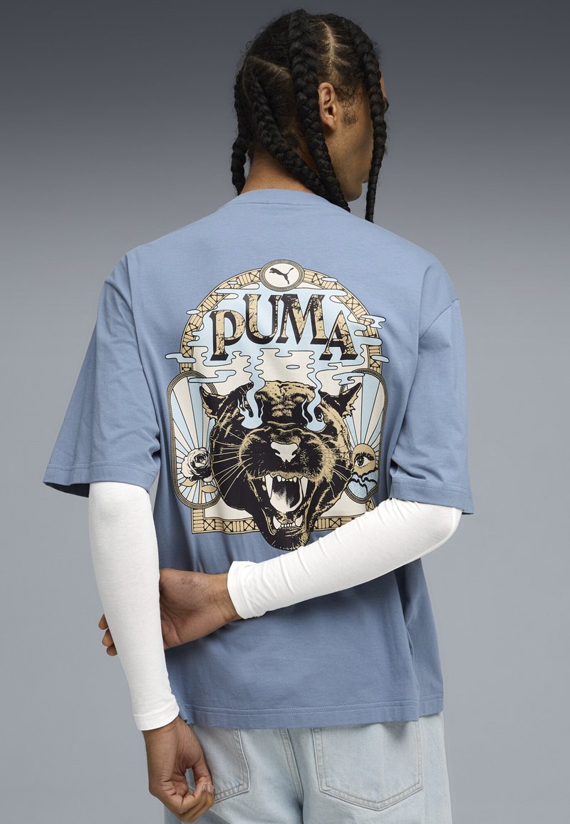 Lyseblå T-shirt med korte ærmer, der har et stort grafisk motiv af en brølende sort panter og ordet "PUMA" i en vintage stil.