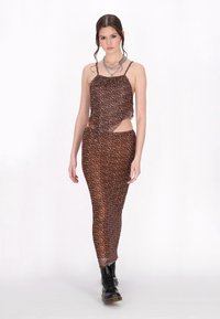 Leopardmönstrad klänning med utskärningsdesign, med bruna nyanser och genomskinligt tyg. Modellen bär den med svarta ankelskot. 