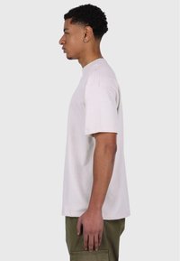 Camiseta corta de manga corta de color beige claro, con cuello redondo, hecha de algodón, con un corte ajustado. Diseño simple y textura suave, vista de lado.