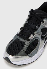 Black athletic shoe featuring a mesh upper, metallic silver accents, a textured finish, and a white rubber sole with black tread.