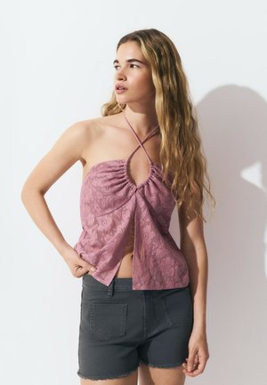 Top halter de color rosa claro con volantes y diseño de abertura, hecho de tela de encaje; combinado con pantalones cortos de mezclilla gris oscuro.