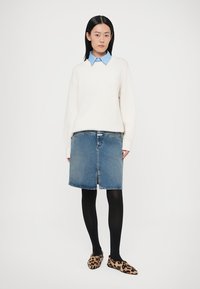 Fehér pulóver, világoskék galléros ing alatt, farmer A-vonalú szoknya, fekete harisnya és leopárdmintás bebújós cipő.