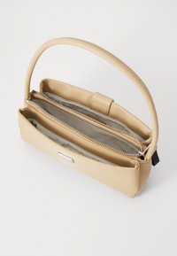 Bolso de mano sintético beige con una textura suave, que presenta una forma estructurada, un asa única y dos compartimentos con cremallera.