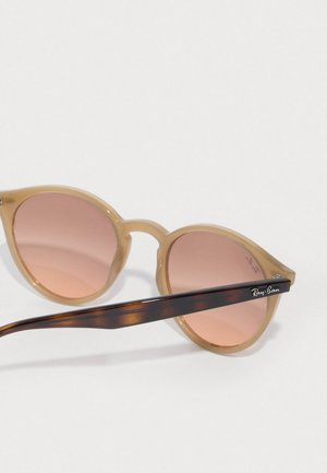 Ray-Ban saulesbrilles ar gai béžam plastmasas kājām un rozā gradienta lēcām. Bruģa lameļu rokai ir sudraba logo detaļa.