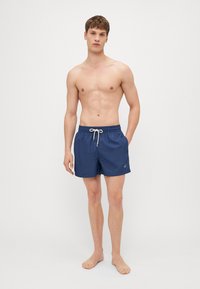 Marineblaue Schwimmshorts mit einem Kordelzugbund, seitlichen Taschen, leichtem Stoff und einem kleinen Logo am linken Bein.