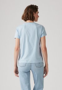 T-shirt in cotone azzurro chiaro con maniche corte, scollo rotondo e una texture semplice e liscia. Indossato con jeans in denim chiaro, vista dal retro.