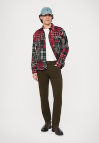 Κόκκινο και μαύρο καρό φλάνελ πουκάμισο με σχέδιο paisley, λευκό t-shirt, σκούρα πράσινα παντελόνια και μαύρες μπότες. Ανοιχτό μπλε καπέλο. Υφασμάτινη υφή.