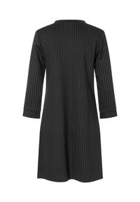 Zwarte jurk met verticale witte strepen, lange mouwen en een hoge halslijn. De stof lijkt glad met een iets losse pasvorm.