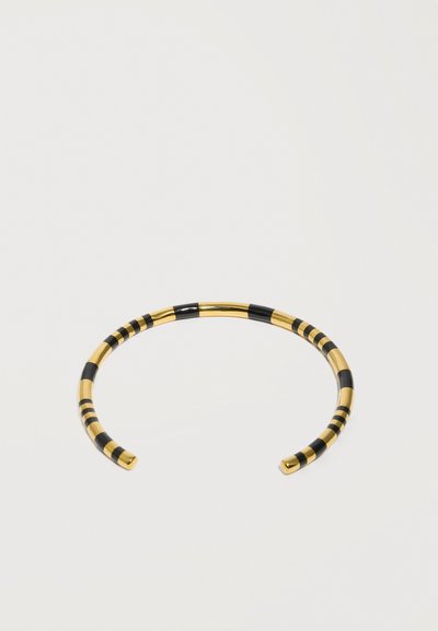 Bracelet manchette en métal doré ouvert, avec des rayures alternées en émail noir sur un fond blanc uni.