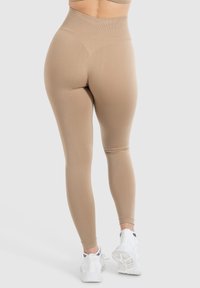 Beige højhals leggings med en glat tekstur, fuldlængde design og ribbet talje, parret med hvide atletiske sko.