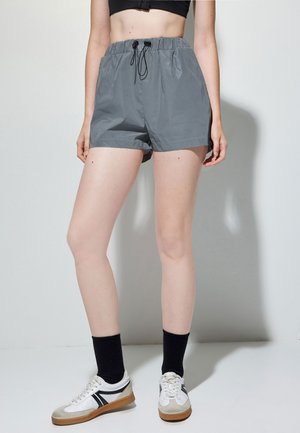 Grå elastiske shorts med strammesnøre, fremstillet af let materiale, med sidelommer og en løs pasform. Sammen med hvide sneakers.