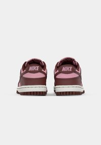 Sapatilhas Nike castanhas e rosas com colarinho almofadado, parte superior em couro e sola de borracha texturizada, apresentando um logótipo distintivo no calcanhar.