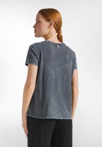Grijs T-shirt met mineraalwas-effect, een ontspannen pasvorm, korte mouwen en een ronde halslijn. Heeft een klein label aan de achterkant bij de halslijn.