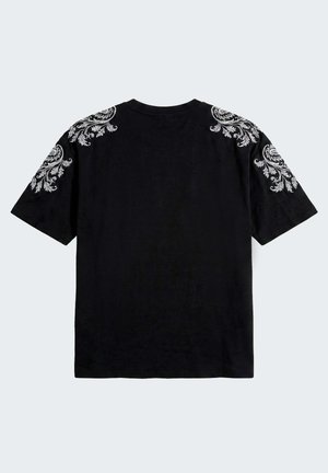 T-shirt nera a maniche corte con ricamo floreale bianco intricato sulle spalle e sulle maniche superiori, vista da dietro su uno sfondo chiaro e semplice.
