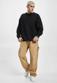 Sort sweatshirt med rund halsudskæring, parret med tan cargo-bukser med lommer og hardware-detaljer, suppleret med hvide sneakers.