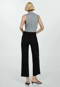 Top gris sin mangas con un cuello alto, combinado con jeans de pierna ancha negros con dobladillos desgastados y detalles de diseño minimalistas.