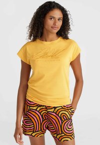 T-shirt giallo a maniche corte con testo in rilievo. Abbinato a pantaloni corti a fantasia con audaci vortici multicolori in rosa e arancione.