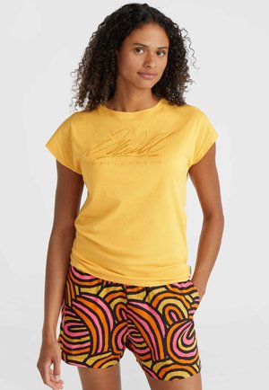 Gelbes T-Shirt mit kurzen Ärmeln und geprägtem Text. Kombiniert mit gemusterten Shorts, die auffällige, mehrfarbige Wirbel in Pink und Orange zeigen.
