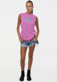 Pink sleeveless t-shirt featuring a blue eagle graphic, paired with distressed denim shorts and black combat boots.