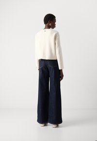 White cropped jacket with a raw hem, paired with wide-leg dark denim pants. The outfit features subtle stitching and button details.