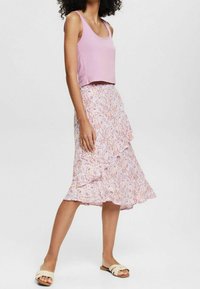 Top corto rosa chiaro abbinato a una gonna fluente e patterned con disegni floreali in rosa, giallo e bianco, rifinita con un bordo arricciato.