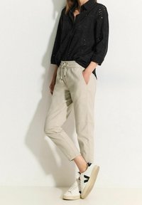 Svart, broderad skjorta med knäppning och avslappnad passform. Ljusbeige, avsmalnande byxor med elastisk midja. Vita sneakers med svarta detaljer.