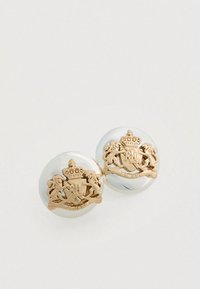 Narukvice u obliku okruglog srebrnog luka s toniranim zlatnim grbom lava i krune, koje sadrže detaljan gravirani i glatku metalnu površinu.