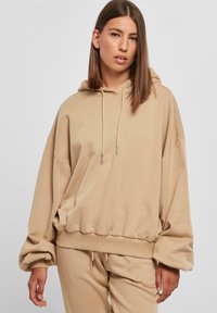 Beige, oversized kapucnis pulóver, húzózsinórral, bordázott mandzsettákkal és texturált felülettel. Lazább szabású és pulóver kialakítású.