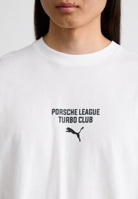 Hvid bomulds T-shirt med en sort grafisk print af "PORSCHE LEAGUE TURBO CLUB" og et springende Puma-logo under teksten.