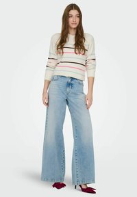 Hvit stripete genser med blå, rosa og brune linjer, kombinert med lyseblå vidbukser og burgunder hælede sko med sløyfer.