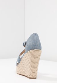 Niebieskie denimowe sandały na koturnie z plecioną platformą z juty, paskiem na kostce i spiczastym nosem. Posiadają metaliczny akcent na obcasie.