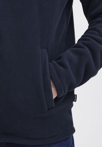 Sudadera de forro polar azul marino con mangas largas, bolsillo lateral, escote redondo y un tejido texturado. La etiqueta muestra la marca "Blend".