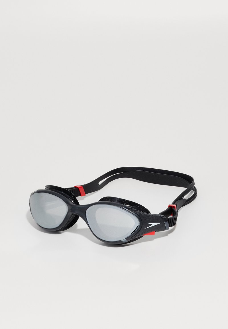 Black swimming goggles with grey lenses, adjustable black strap, and red accents. Features a sleek design and textured sides for grip.