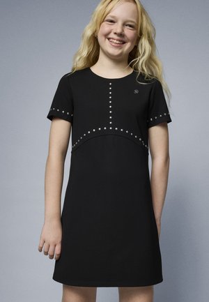 Vestido negro de manga corta con escote redondo, detalles con tachuelas en el cuerpo y las mangas, presentando un sutil diseño curvado.