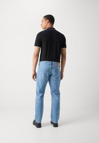 T-shirt polo noir avec des accents blancs, associé à un jean droit bleu clair. Des chaussures noires complètent la tenue.