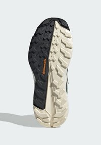 Zool van een schoen met zwarte rubberen en crèmekleurige secties, voorzien van een textuurpatroon voor grip en een oranje logo in het midden.