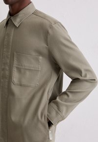 Olivgrünes Hemd zum Knöpfen aus glattem Stoff; mit Brusttasche und Anhänger. Klassischer Kragen und schlanke Passform.