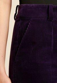 Lila kordflorskjol med vertikalt ribbad textur, hög midja och sidofickor. Tyget ser mjukt och något glänsande ut.