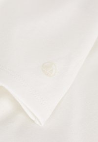 Weißes Baumwoll-T-Shirt mit einem dezenten, geprägten Logo am Ärmel. Der Stoff hat eine glatte Textur und saubere Nähte.