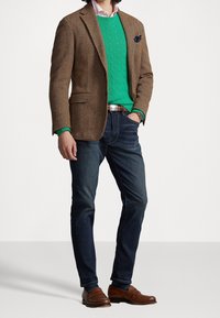 Brun blazer i sicksackmönster, grön kabelstickad tröja, ljusrosa skjorta, mörka jeans, bruna loafers med liten spänndetalj.