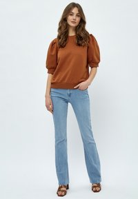 Brun sweatshirt med puffärmar och ribbad nederkant, kombinerad med ljusblå raka jeans och bruna sandaler med remmar.