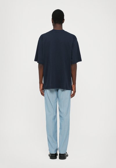 Marinblå bomullströja med korta ärmar, i kombination med ljusblå randiga byxor, designade för en avslappnad passform. Enkel och minimalistisk look.