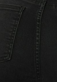 Primer plano de una tela de mezclilla negra que muestra un bolsillo trasero y una costura detallada a lo largo de la costura.