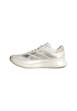 Zapatilla para correr blanca y beige de perfil bajo con parte superior de malla, tres franjas plateadas en el lateral y una suela gruesa acolchada con suela de goma.