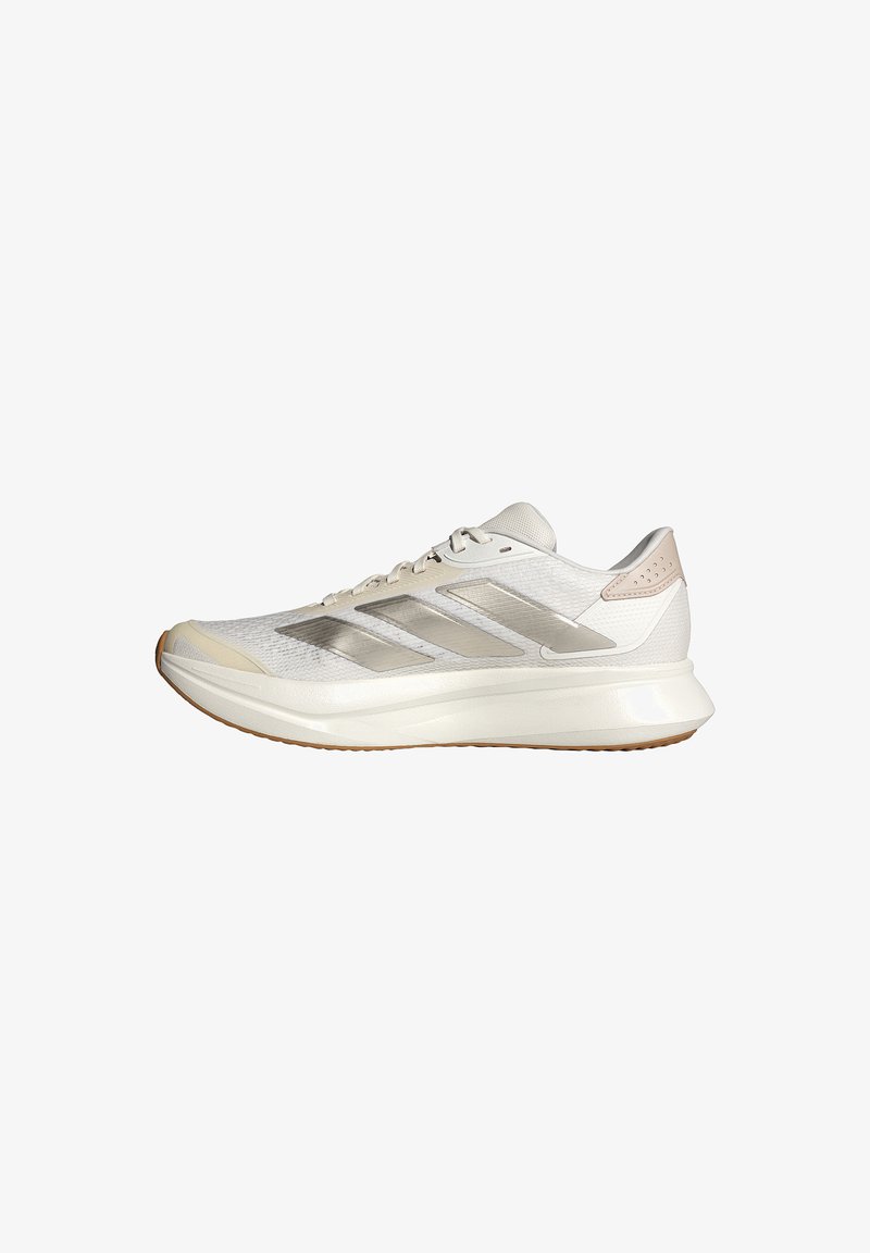 Chaussure de course basse blanche et beige avec une tige en mesh, trois bandes argentées sur le côté et une semelle épaisse et rembourrée avec une semelle extérieure en gomme.