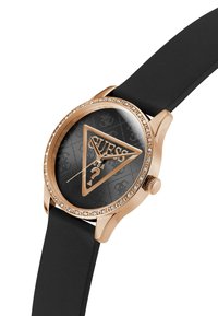 Reloj de oro rosa con una esfera negra que presenta un logotipo triangular y acentos de cristal, montado en una correa de silicona negra. Caja metálica redonda.