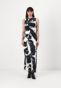 Rochie fără mâneci, cu imprimeu tie-dye alb-negru, cu un design ajustat, până la genunchi, și un detaliu răsucit pe lateral. Puritată cu cizme negre până la gleznă.