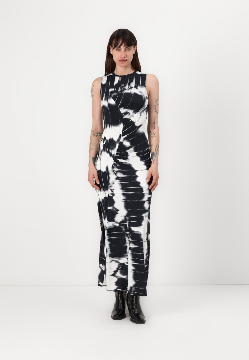Rochie fără mâneci, cu imprimeu tie-dye alb-negru, cu un design ajustat, până la genunchi, și un detaliu răsucit pe lateral. Puritată cu cizme negre până la gleznă.