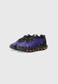 Ténis Nike com um design em roxo e preto, tecido texturizado, sola de borracha lisa e distintivas pérolas de amortecimento laranja.
